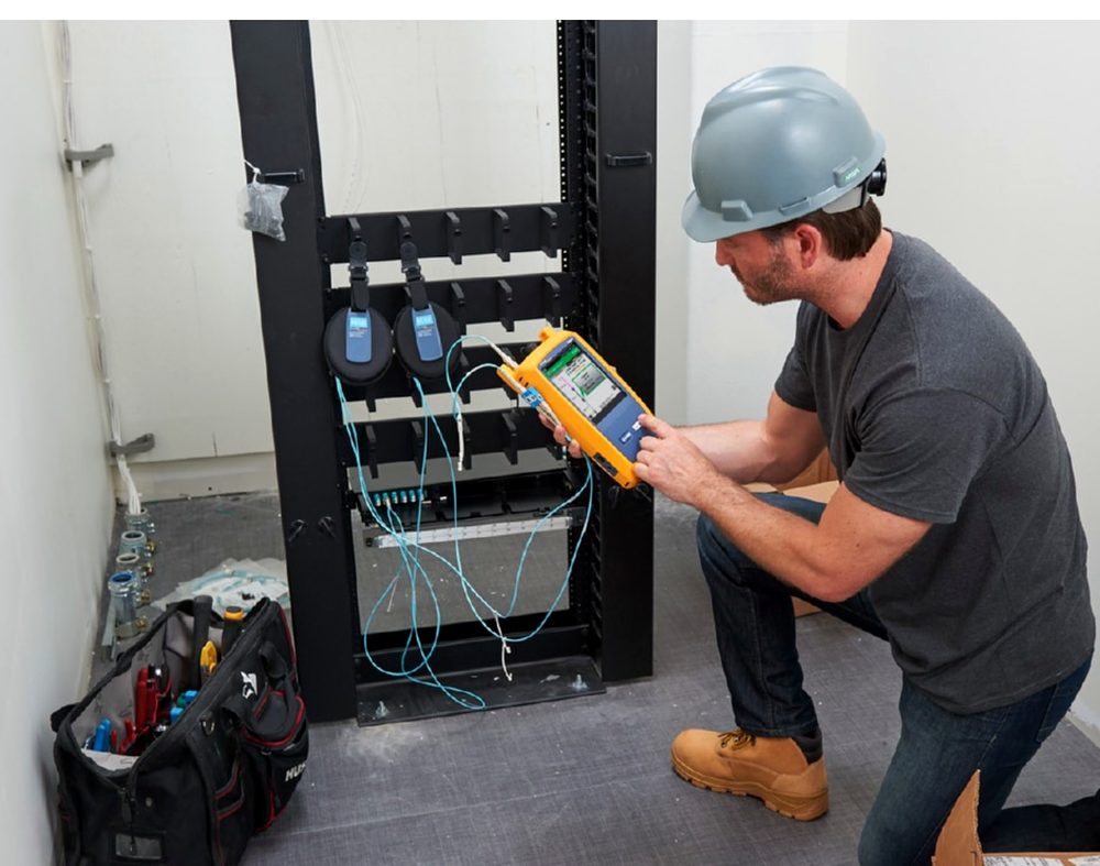 Technicien certifiant les prises RJ45 d'une baie de brassage avec un testeur de certification Fluke Networks