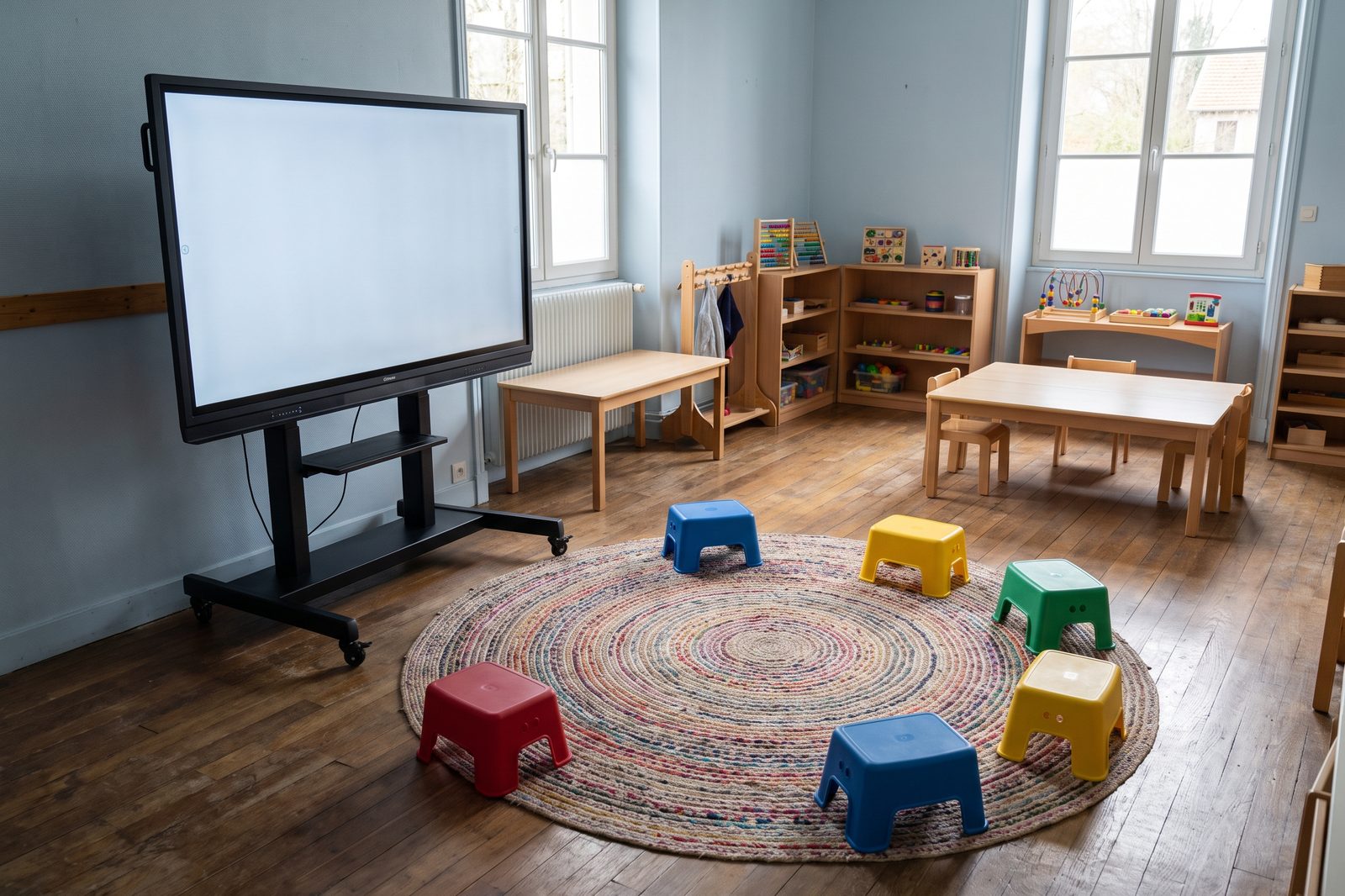 Salle de classe de maternelle &eacute;quip&eacute;e d'un &eacute;cran interactif sur colonne mobile, descendu &agrave; hauteur d'enfant